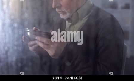 Upset poor senior man looking at bowl with tasteless food, low social help Stock Photo
