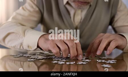 Male pensioner assembling jigsaw puzzle at home, alzheimer rehabilitation, hobby Stock Photo