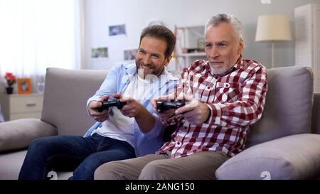 Senior male with son playing video game using joystick, having fun together Stock Photo