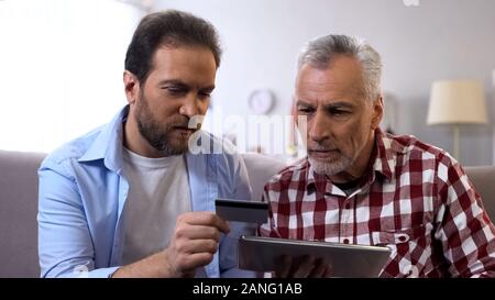 Son teaching father how to book tickets online, using tablet and credit card Stock Photo