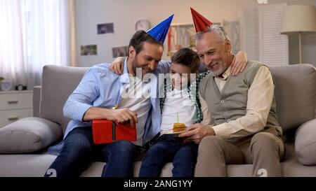 Granddad and dad congratulating preteen boy on b-day, giving gift box and cake Stock Photo