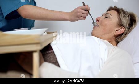 Nurse feeding disabled mature woman with porridge, care for patients, hospice Stock Photo