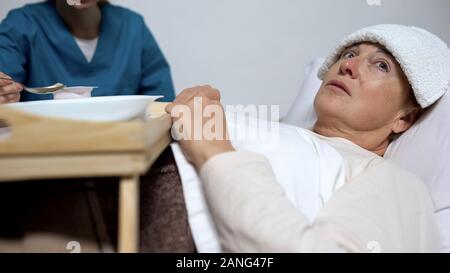 Sick-nurse feeding disabled woman with compress on forehead, hopelessness Stock Photo