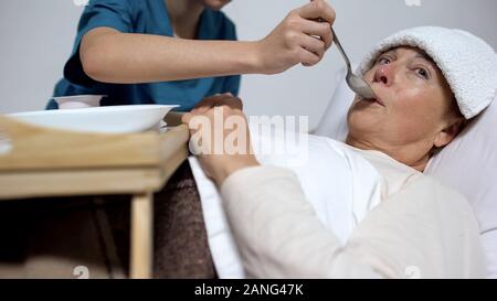 Nurse of mental hospital feeding indifferent woman with porridge, asylum Stock Photo