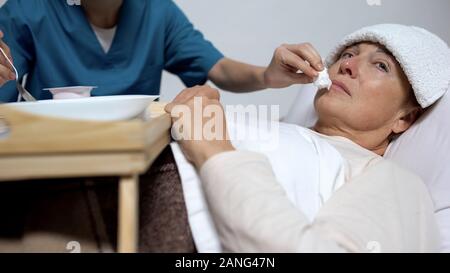 Hospice worker helping to eat mentally disabled elderly woman, healthcare Stock Photo