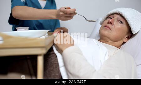 Terminally ill woman looking at camera, nurse feeding patient, Alzheimer disease Stock Photo