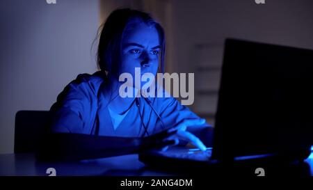 Concentrated doctor working on laptop at night, filling medical card of patient Stock Photo