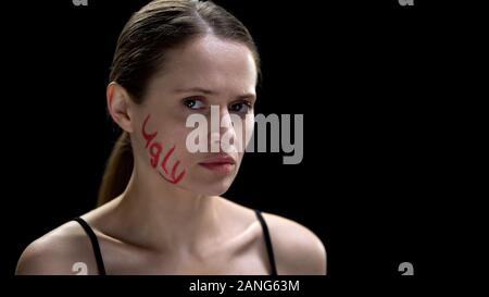 Upset woman with ugly word written on cheek looking at camera, low self-esteem Stock Photo