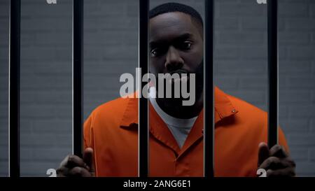 Black male prisoner waiting for sentence in prison cell, looking sadly to camera Stock Photo