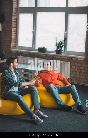 Nice joyful friends sitting in the beanbag chairs Stock Photo