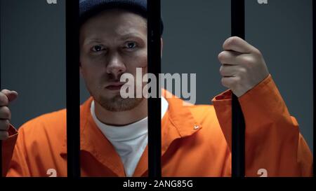 Disappointed criminal with scar on face holding prison bar, looking at camera Stock Photo