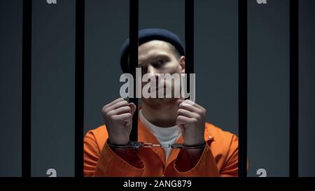 Dangerous arrogant prisoner standing behind bars and showing handcuffed hands Stock Photo