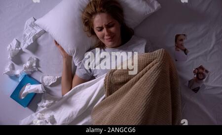 Woman crying lying in bed with tissues, torn photo of ex-boyfriend beside, break Stock Photo