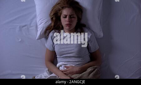 Lady feeling sharp lower abdominal pain during sleeping, suffering from cystitis Stock Photo
