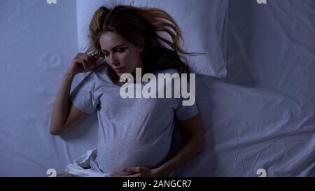 Exhausted pregnant woman lying in bed, thinking about motherhood, top-view Stock Photo