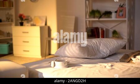 White alarm clock lying on messy bed, crumpled bed sheets, oversleeping concept Stock Photo