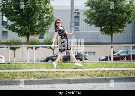 Adult brunette woman running down the street in a stylish dress. The concept of the style of life, urban, happiness and active life. Stock Photo