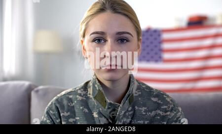 Sad female soldier in camouflage uniform looking at camera, USA flag background Stock Photo