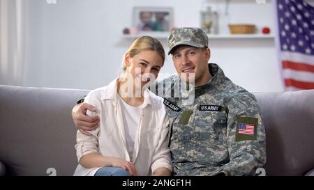 Happy US army soldier hugging wife sitting on sofa and smiling at camera, nation Stock Photo