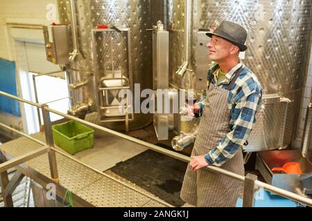 Winemaker with a glass of red wine in the winery in front of a fermentation tank Stock Photo
