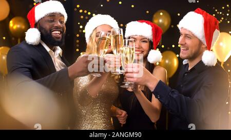 Multiracial friends in santa hats clinking champagne glasses, New Year party Stock Photo