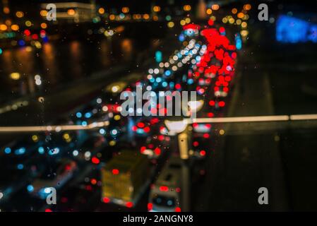 Night road with blurry cars and headlights. Car traffic shot through glass, focusing on raindrops. Rainy and cloudy day Stock Photo