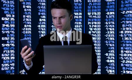 Man in suit with laptop checking information on smartphone, digital data Stock Photo