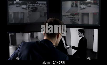 Security operator watching transfer of bribe on CCTV footage, safety concept Stock Photo