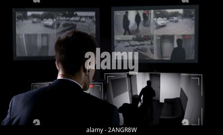 Security guard in earphones watching robbery attempt on surveillance cameras Stock Photo