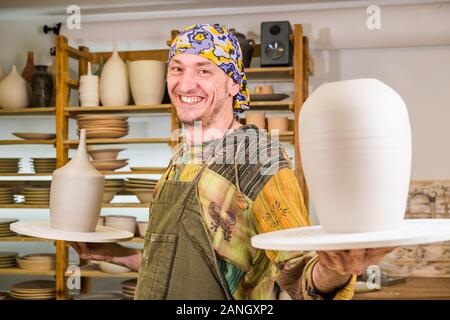 Smiling male potter master holding pottery art products in his workshop, small art business concept Stock Photo