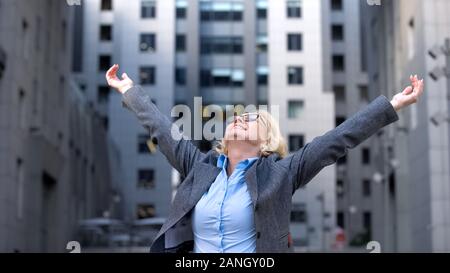 Smiling aged female worker looking up raised hands, freedom happiness, goal Stock Photo