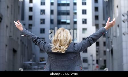 Carefree blond woman in formal suit raised up hands back view, female wellness Stock Photo