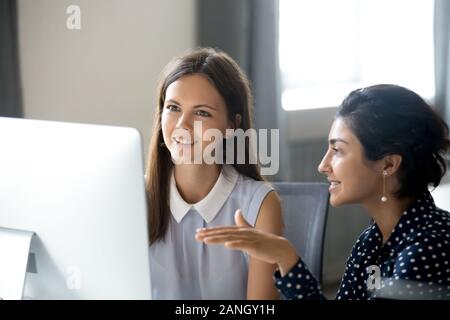 Smiling multiracial millennial women work on computer in office together, discuss startup project, diverse young female colleagues talk explain ideas, Stock Photo