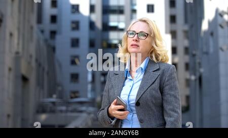 Worried company manager holding smartphone thinking of work problem outdoors Stock Photo