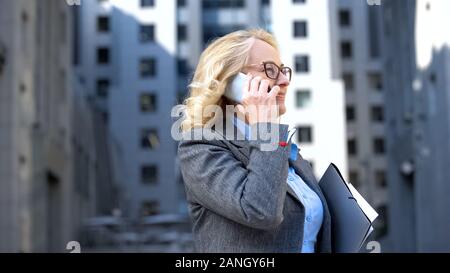 Happy female manager talking phone with business partner holding documents Stock Photo