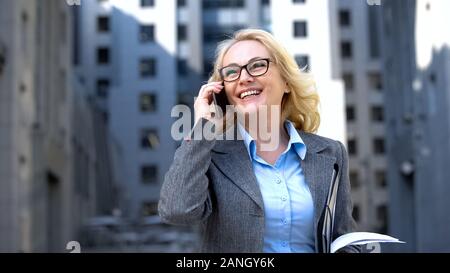 Successful business lady with documents in hand talking phone and smiling, work Stock Photo