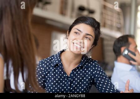Close up of smiling millennial girl talk with female colleague, explain work issue or chat at break, happy woman worker speak with coworker in shared Stock Photo