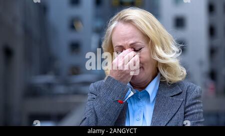 Desperate aged woman in business suit crying outdoors office building, dismissal Stock Photo