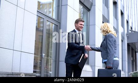 Happy business partners shaking hands outdoors, male and female colleagues Stock Photo