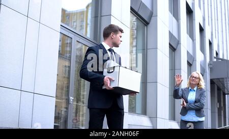 Sad male manager with stuff box looking gloating female boss, company dismissal Stock Photo