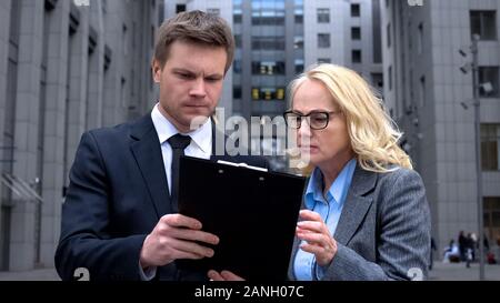 Concentrated male and female colleagues reading document together outdoors Stock Photo