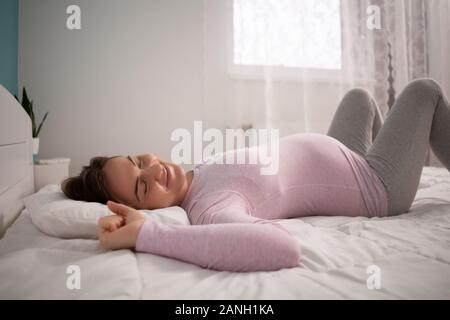 Pregnant woman is sleeping and stretching in her bed.
