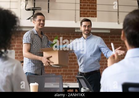 Millennial boss or CEO introduce excited male newbie holding box with belongings to company workers, employer acquaint team with new colleague, welcom Stock Photo