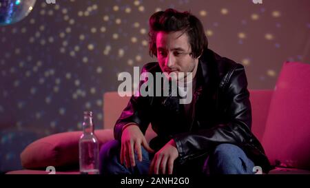 Drunk man looking at vodka bottle in night club, unhealthy lifestyle concept Stock Photo