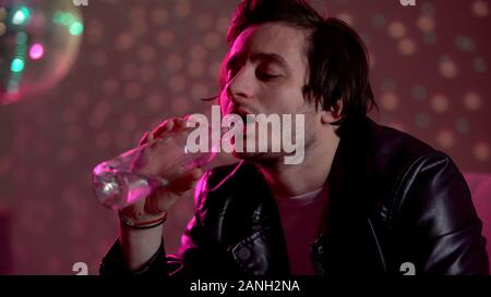 Man drinking vodka from bottle at party, suffering depression, alcohol addiction Stock Photo