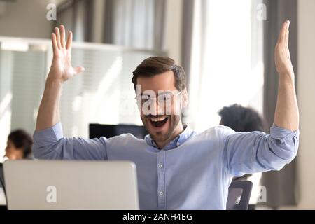 Excited male employee look at screen scream with happiness witness sales rising or project success, happy man worker gesture yes winning lottery onlin Stock Photo