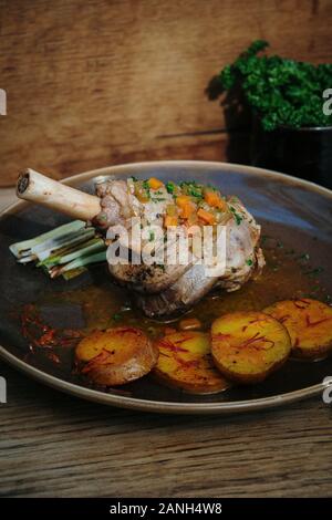 Roast dinner. Main course of roasted Lamb shank with saffron potatoes and leek, Wooden background Stock Photo