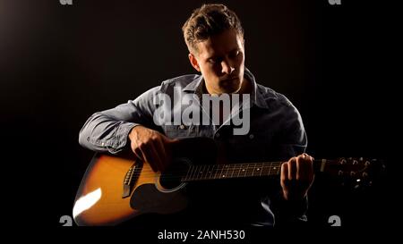 Young man playing romantic ballad on guitar, acoustic performance, concert Stock Photo