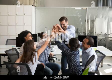 Excited diverse employees give high five motivated for shared goal achievement at informal briefing in office, smiling colleagues join hands involved Stock Photo