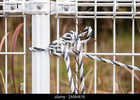 A black and white nylon rope is tied on a white metal fence. Stock Photo